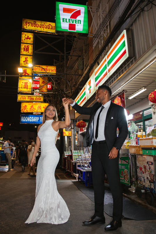 Couple in wedding attire dancing outside a 7-Eleven at night during a Bangkok photoshoot by photographer Nadya Shell.
