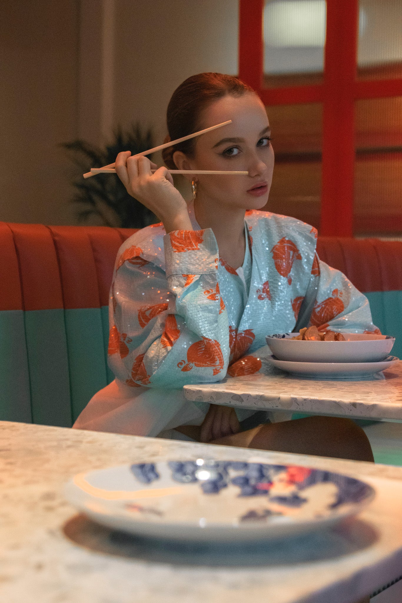 Woman in a colorful outfit sitting at a table with plates and chopsticks in a restaurant setting. Bangkok Chinatown Photoshoot by Photographer Nadya Shell