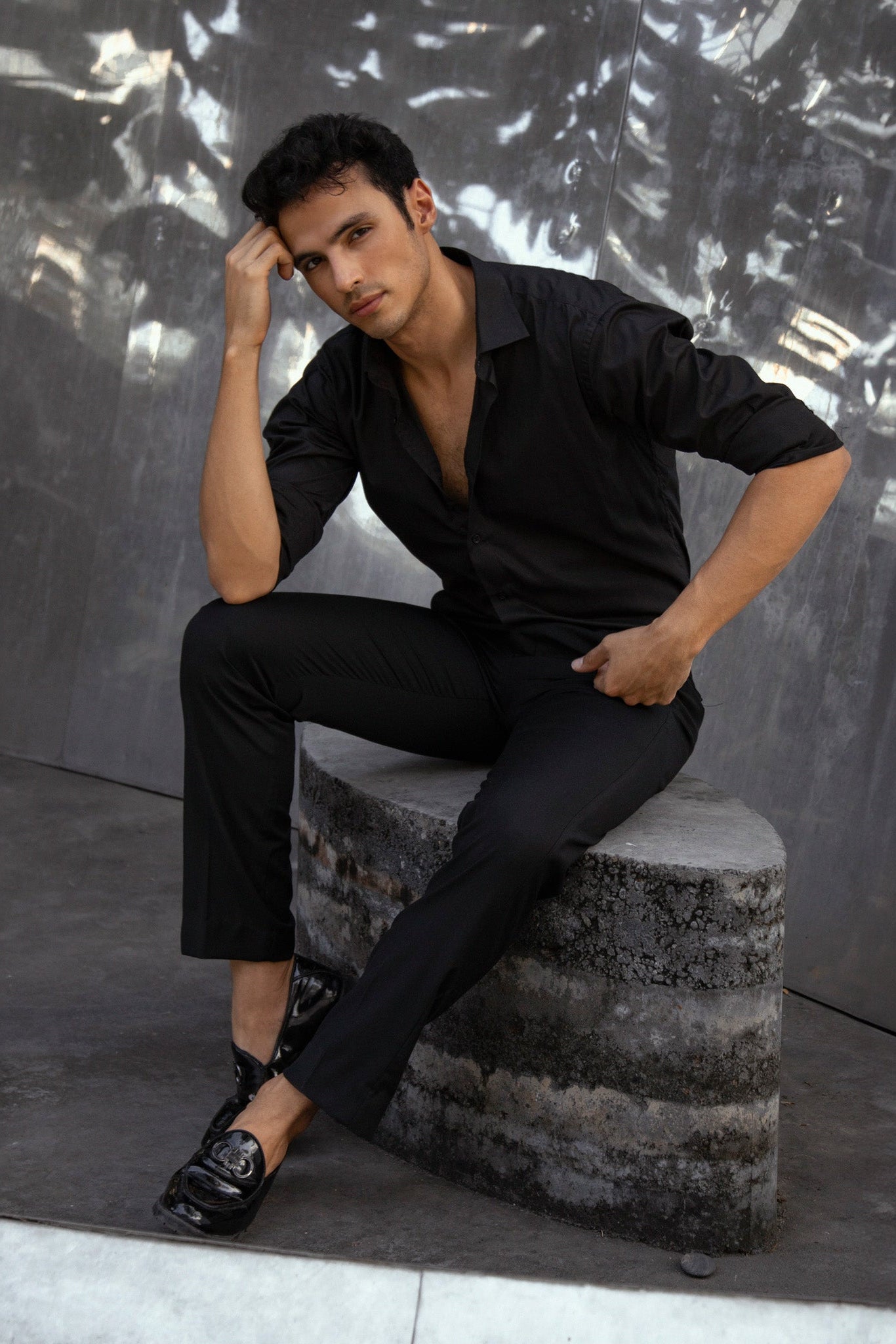 Man in black outfit sitting on a textured block against a reflective metallic wall. Bangkok Photoshoot by Photographer Nadya Shell