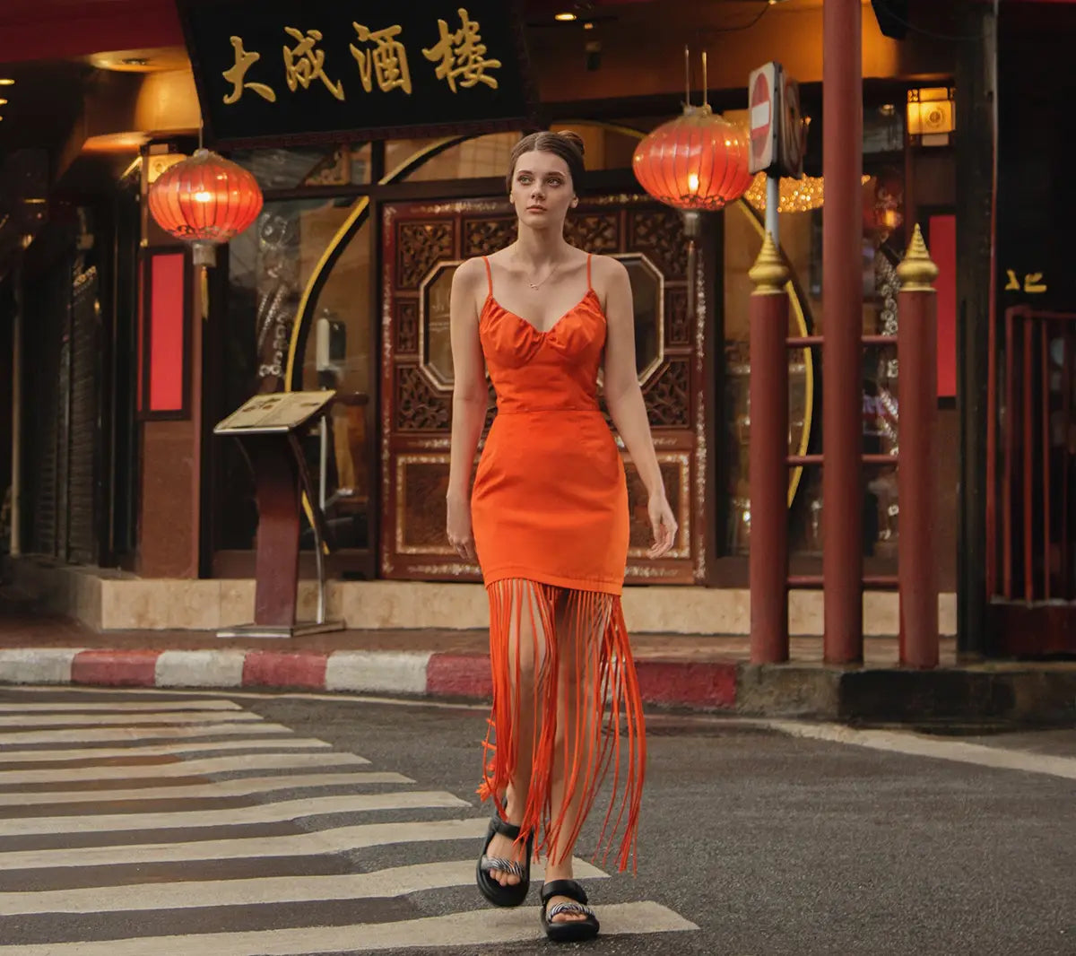 Woman in an orange dress with fringe walking on a street with Chinese restaurant exterior. Bangkok Photoshoot by Photographer Nadya Shell.
