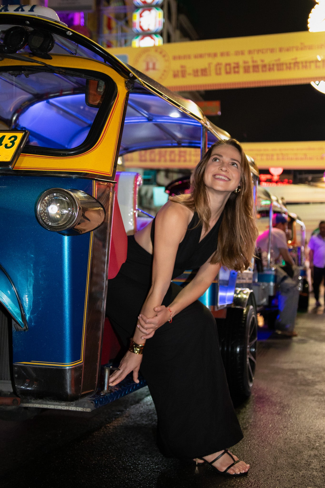 Bangkok Night Chinatown Photoshoot by Photographer Nadya Shell. Woman in a black dress standing next to a colorful tuk-tuk at night.