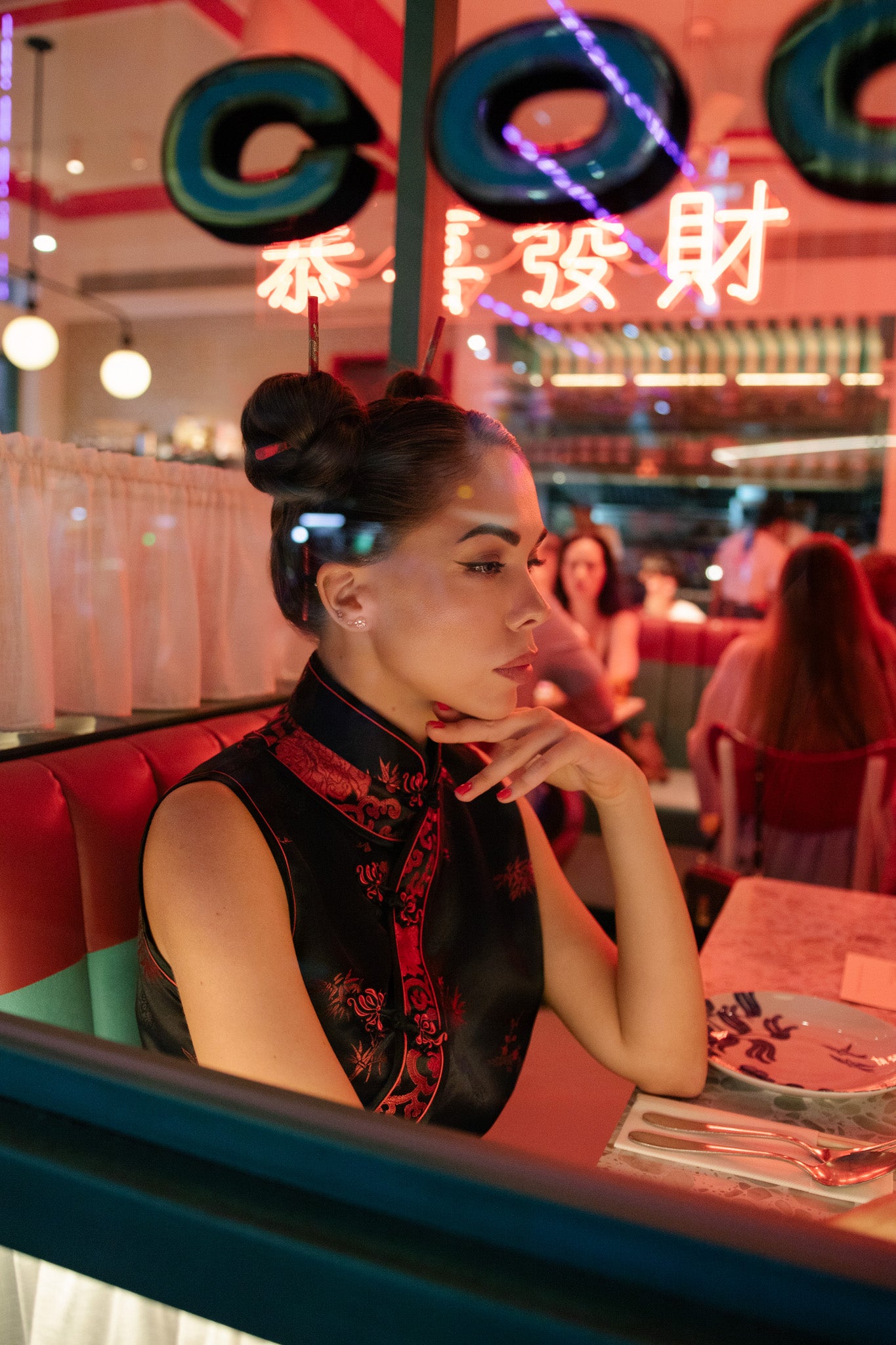 Woman sitting in a diner with neon signs and other patrons in the background. Bangkok Chinatown Photoshoot by Photographer Nadya Shell