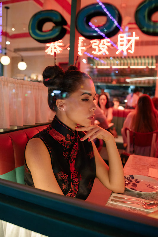 Woman sitting in a diner with neon signs and other patrons in the background. Bangkok Chinatown Photoshoot by Photographer Nadya Shell